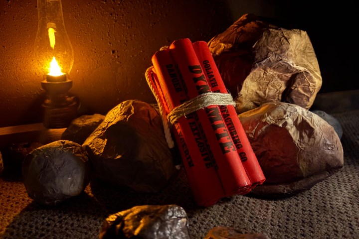 Dynamite sticks tied together next to rocks, lit by an oil lamp.
