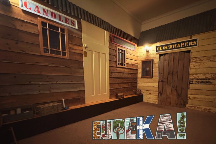 Indoor wooden storefronts labeled Candles, Confectionery, and Clockmakers, with 'Eureka!' logo at the bottom.