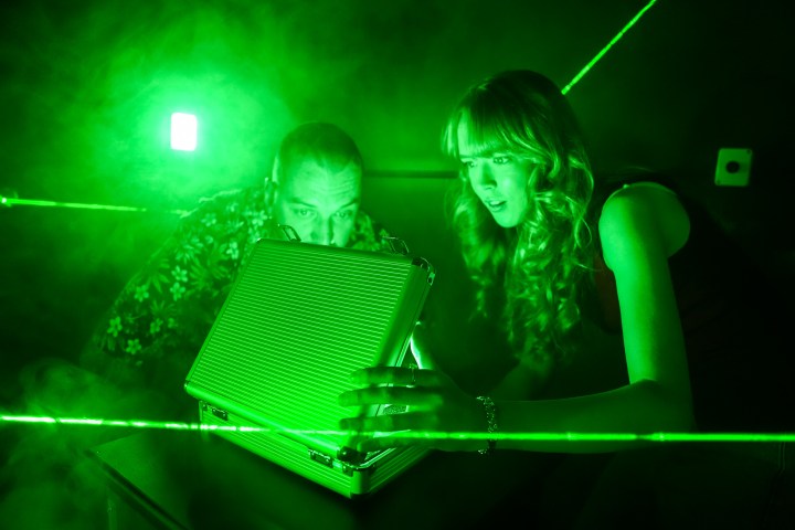 Two people looking at a briefcase in a green-lit room with laser beams.
